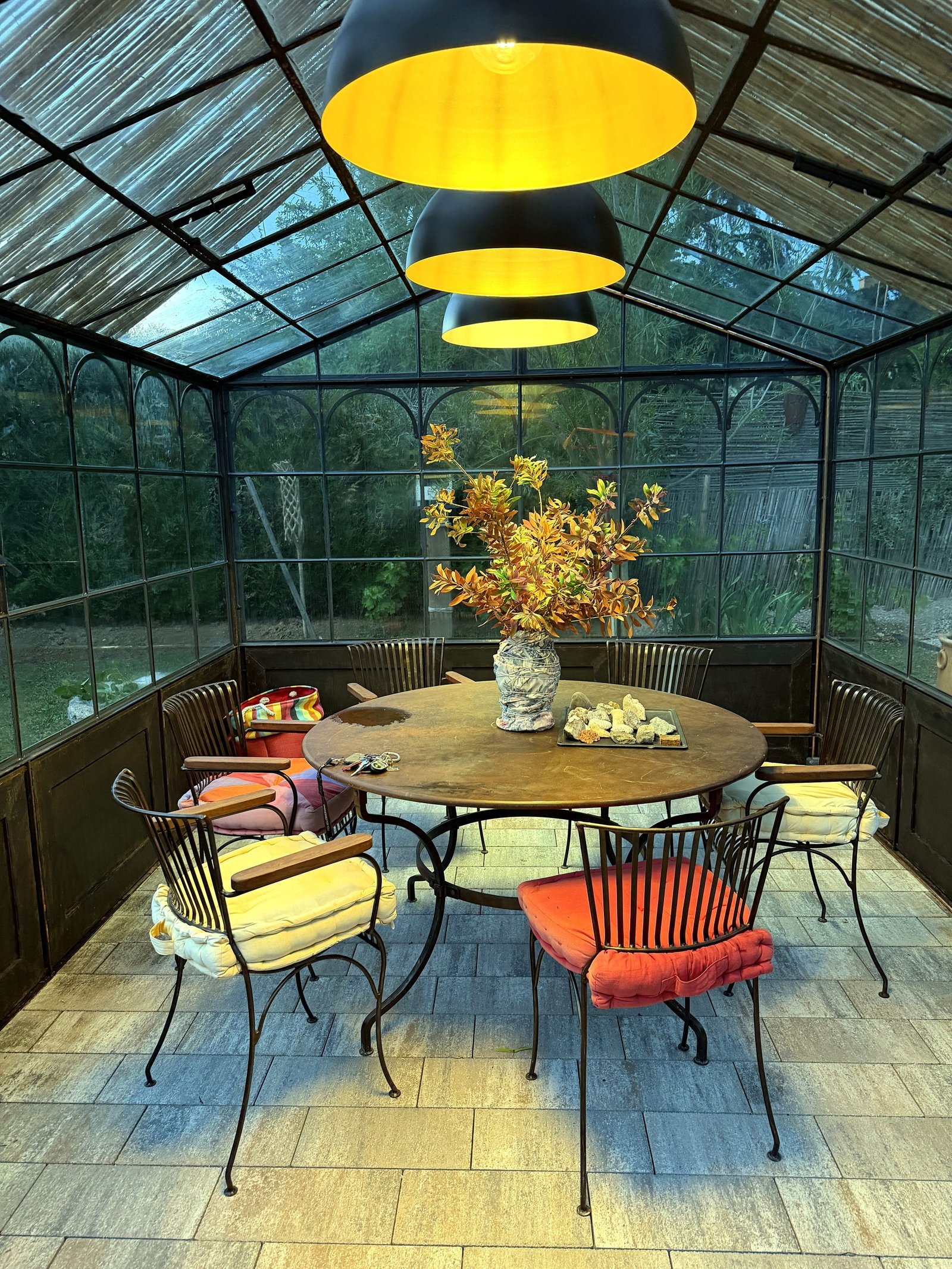 Intérieur d'une serre en fer forgé HD Gloriettes et Compagnie, table dressée et suspensions à la lumière chaude
