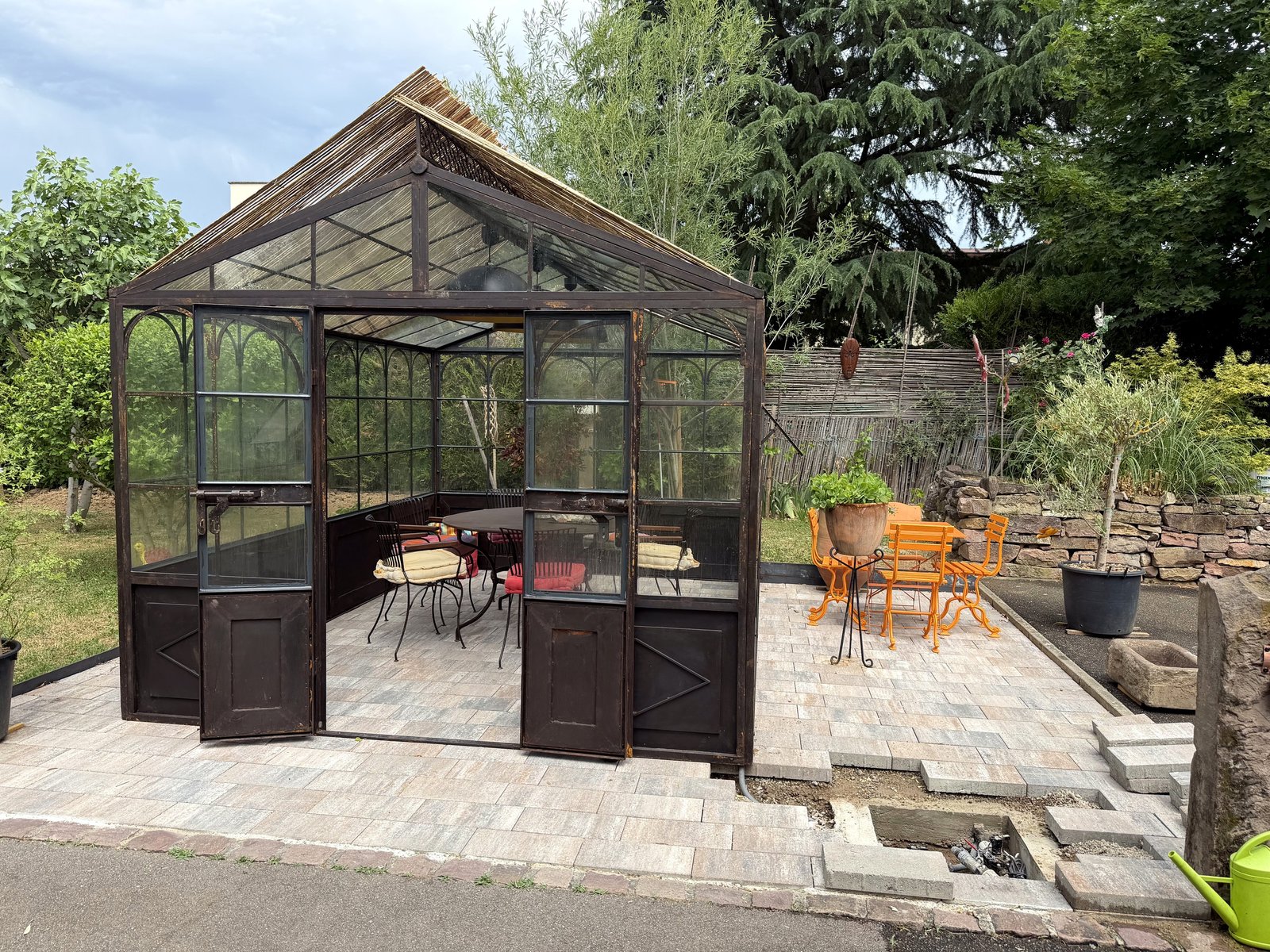 Serre en fer forgé aménagée en salon de jardin, mobilier et plantes