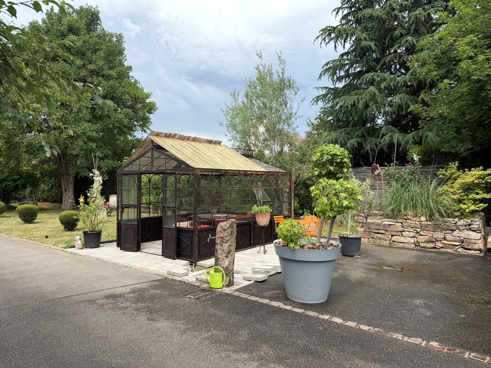 Serre de jardin en fer forgé à l'ancienne, vue de trois quarts dans un jardin